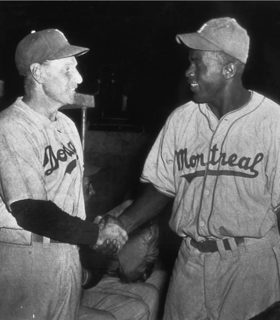 Jackie Robinson shaking hands with Brooklyn Dodgers manager amid a tense crowd.