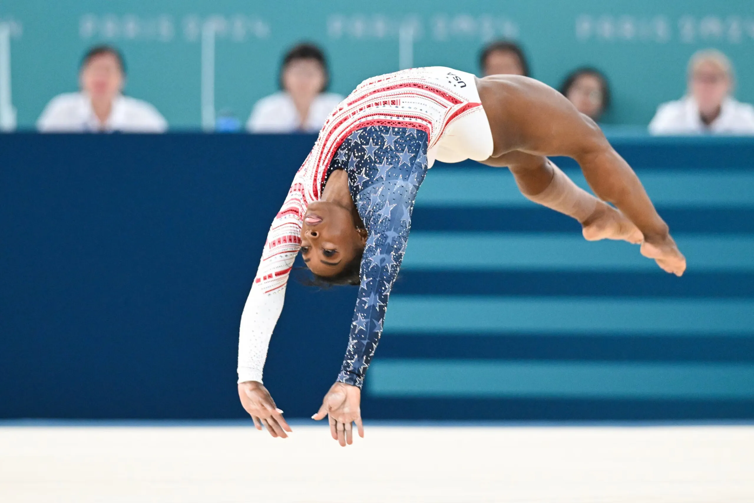 Simone Biles mid-air performing her signature vault, representing the peak of Simone Biles' childhood secret training story